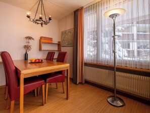 Ein Essbereich mit einem Holztisch, roten Stühlen, einer Kristallleuchter, einer Stehlampe und einem fenster mit Vorhängen.