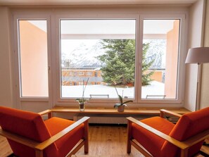 Ein Zimmer mit einem großen Fenster, zwei orangefarbenen Stühlen, einem kleinen Tisch und einer Heizung.