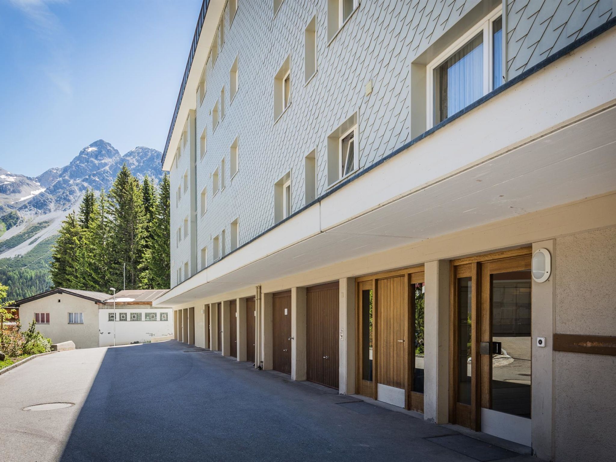 Um hotel com uma fileira de quartos, uma galeria coberta e vista para as montanhas ao fundo.