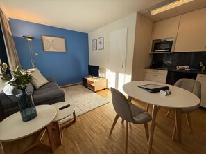A modern living room with a blue accent wall, a grey sofa, a coffee table, and a dining area with a white table and chairs. - Waldhof 1 by Arosa Holiday Appartement/Fewo, Dusche, WC, 2-Bettwohnung Waldhof 1 by Interhome (Arosa)