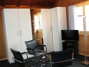 Ein Zimmer mit Fernseher, zwei schwarzen Stühlen und einem Schrank.
