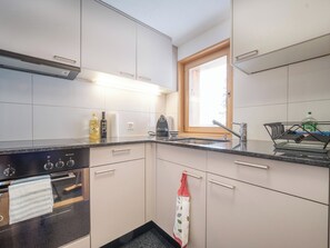 A kitchen with white cabinets, a black stove, a window, and a stainless steel sink. - Chalet Höckli 2 Appartement/Fewo,   4-Bettwohnung by Interhome (Arosa)