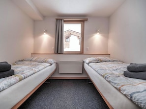 Ein Doppelzimmer mit zwei Betten, einem Fenster mit Vorhängen, einem Heizkörper und Blick auf ein Gebäude.