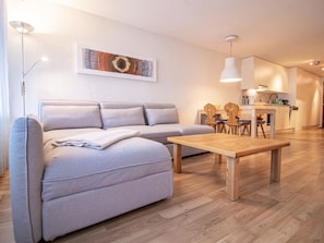 A modern living room with a sofa, a wooden coffee table, and a dining area with chairs and a table. - Rothornblick 57 by Arosa Holiday Appartement/Fewo, Bad, WC, 2-Bettwohnung by Interhome (Arosa)