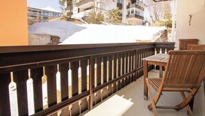 Een balkon met houten hekwerk, een houten stoel en uitzicht op een gebouw met sneeuw op het dak.
