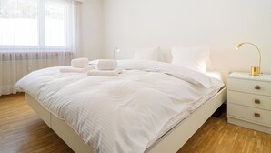 Een slaapkamer met een groot bed, nachtlampjes en een raam met dunne gordijnen.
