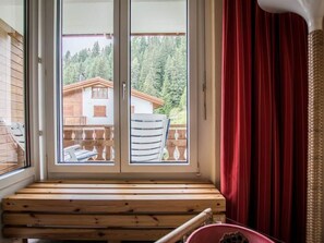 A room with a wooden bench, a red curtain, and a view of a house through a glass door. - Chalchboda 1 Appartement/Fewo, Bad, WC, 6-Bettwohnung by Interhome (Arosa)