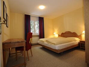 Une chambre d’hôtel avec un lit, des lampes de chevet, un bureau et une chaise.