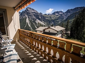 Ein Balkon mit Holzgeländer, einem karierten Kissen und Blick auf die Berge.