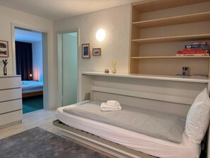 Ein Schlafzimmer mit einem Bett, einem Nachttisch, einer Kommode, einem Bücherregal und einer Wandleuchte.
