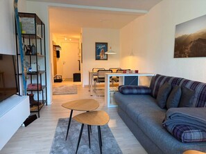 Ein Wohnzimmer mit einer Couch, einem Couchtisch, einem Essbereich mit Stühlen und einem Bücherregal.