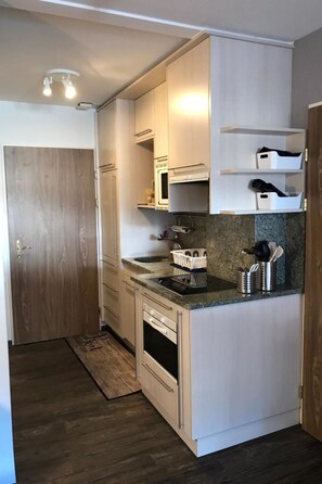 Eine kleine Küche mit weißen Schränken, einem eingebauten Backofen, einer Mikrowelle und einer Arbeitsplatte aus Granit.