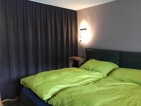 Ein Hotelzimmer mit Bett, Nachttisch, Lampe und einem Fenster mit Vorhängen.