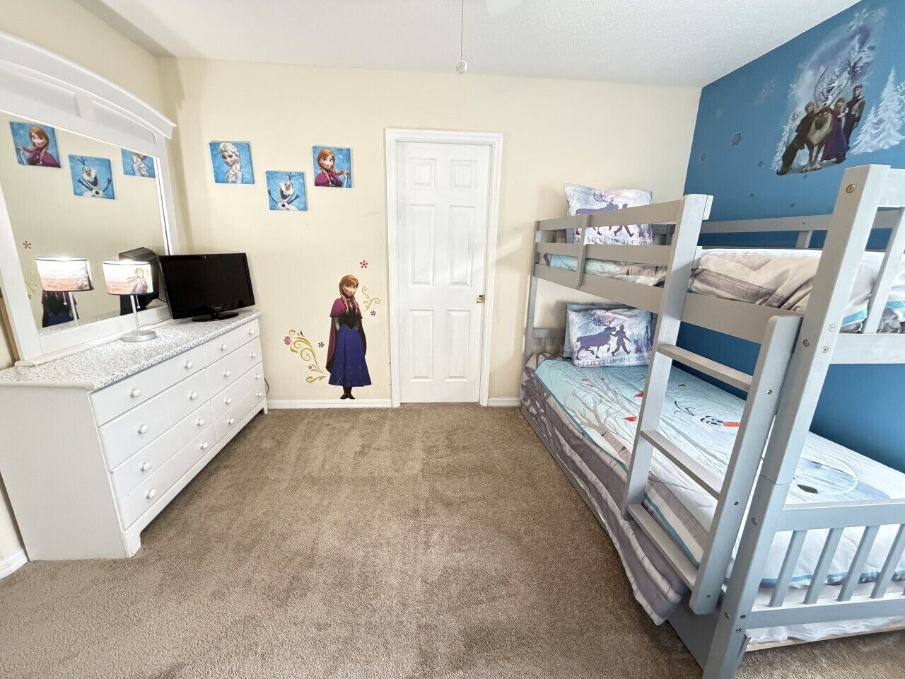 A bedroom with bunk beds, a dresser, a television, and wall decorations.