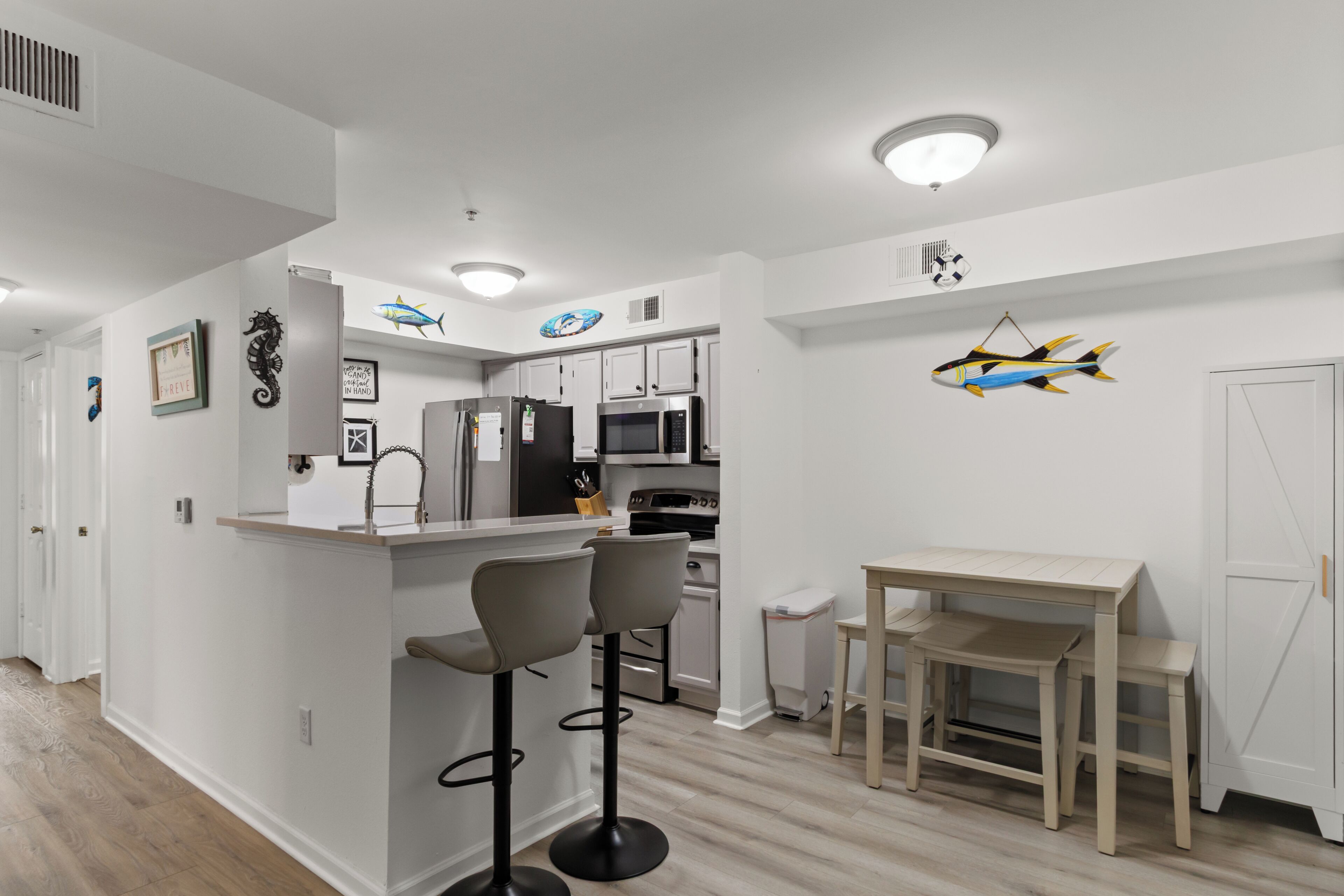 A modern kitchen with white cabinets, a central island with bar stools, a microwave, and a refrigerator.
