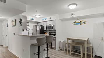 A modern kitchen with white cabinets, a central island with bar stools, a microwave, and a refrigerator.