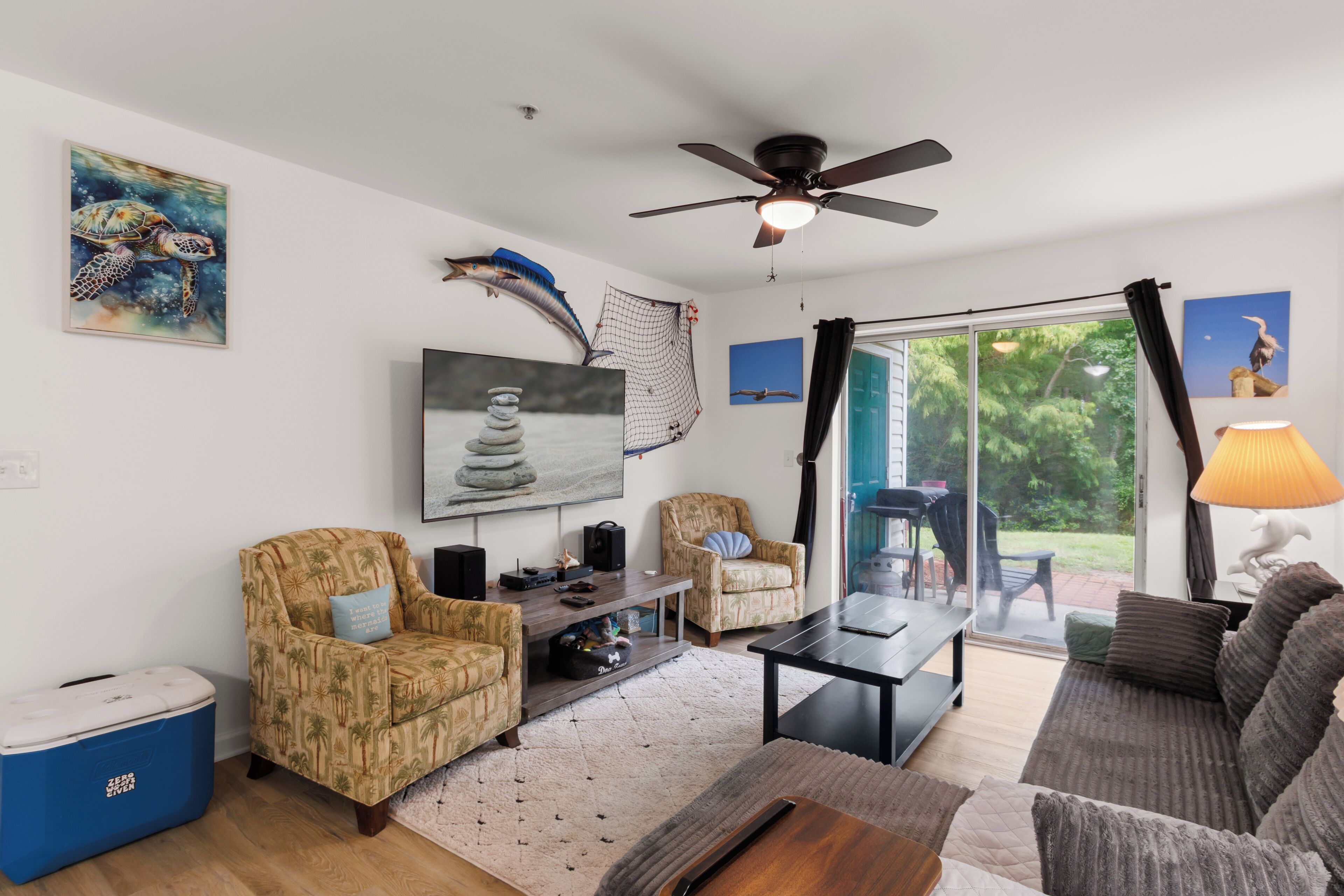 A living room with a ceiling fan, a TV, a sofa, a coffee table, and a large window with curtains.