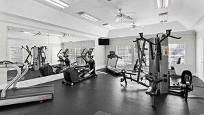 Ein Fitnessstudio mit verschiedenen Trainingsgeräten, Spiegeln, Deckenventilatoren und einem Fernseher.