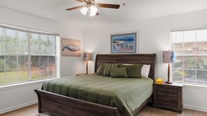 Ein Schlafzimmer mit einem Bett, Deckenventilator, zwei Nachttischen und großen Fenstern.