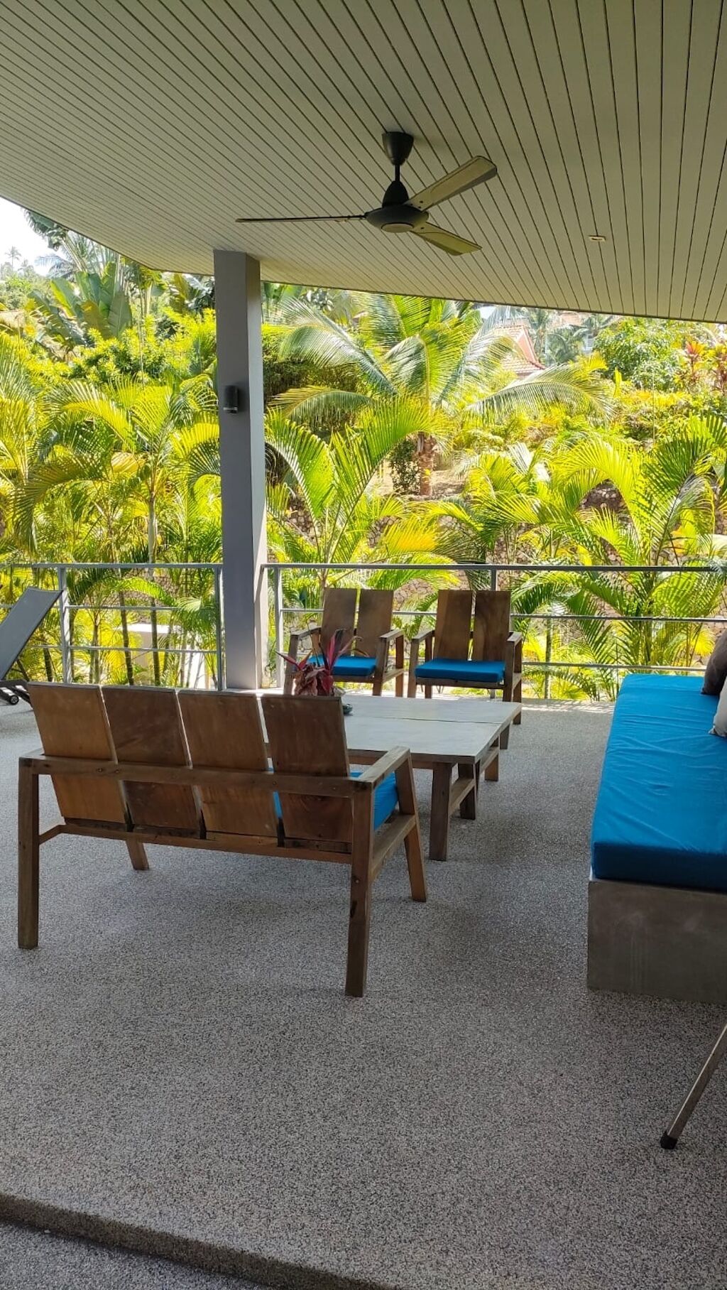 A covered outdoor seating area with wooden furniture and a view of lush greenery.