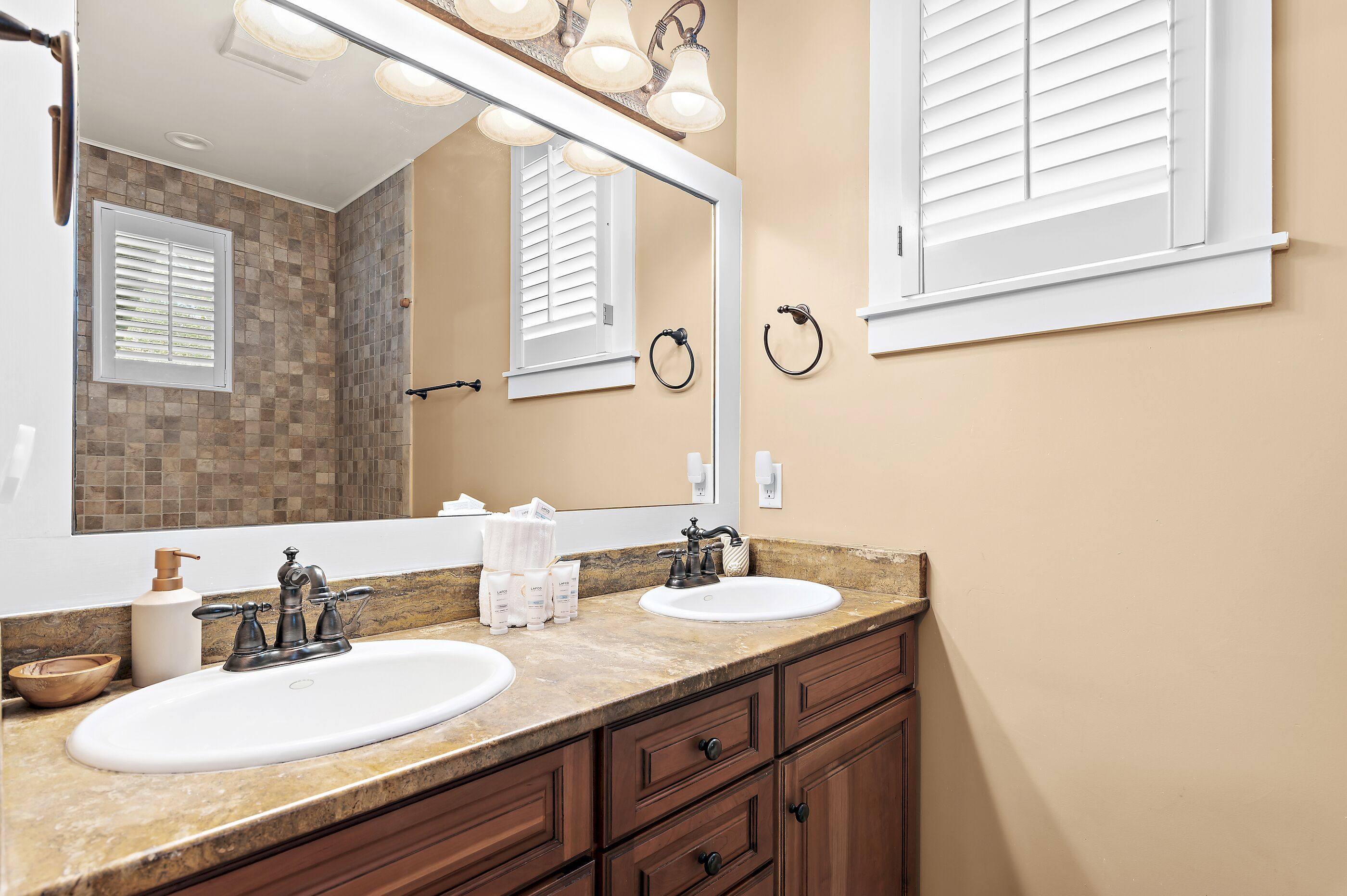 A bathroom with two sinks, a large mirror, and a window with blinds.