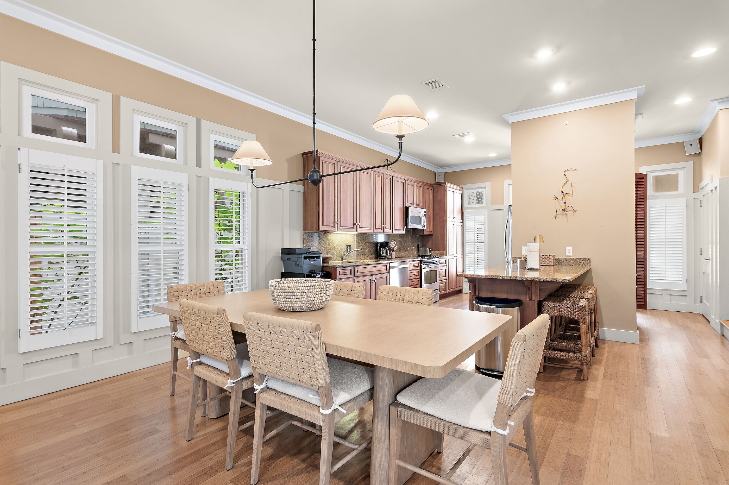 A modern kitchen with wooden cabinets, a dining table with chairs, and pendant lighting.