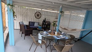 A covered patio area with wicker furniture, a dining table set with blue and white plates, and a hammock.