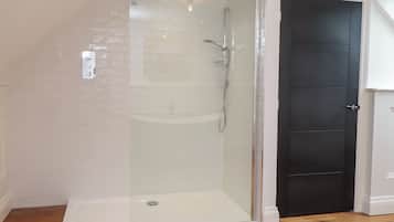 A glass-enclosed shower with a white tiled wall, a dark door, and wooden flooring.