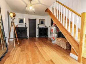 A spacious room with wooden flooring, a staircase with white balusters, and two black cabinets with decorative items.