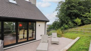 Une maison moderne dotée d’une grande porte vitrée, d’une terrasse carrelée et de mobilier d’extérieur.