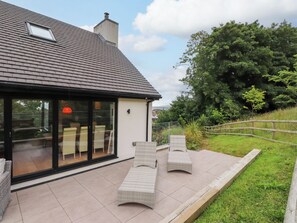 A modern house with a large glass door, a tiled patio, and outdoor furniture. - The Barn at Bryn Eithin (Colwyn Bay)