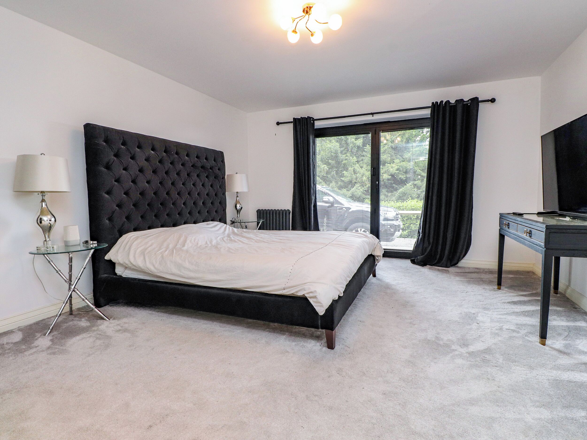 Une chambre avec un grand lit, un bureau, une chaise, une lampe, un radiateur et une vue sur l’extérieur.
