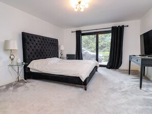 Ein Schlafzimmer mit einem großen Bett, einem Schreibtisch, einem Sessel, einer Lampe, einem Heizkörper und Blick ins Freie.
