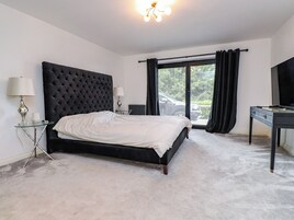 Un dormitorio con una cama grande, un escritorio, una silla, una lámpara, un radiador y vistas al exterior.