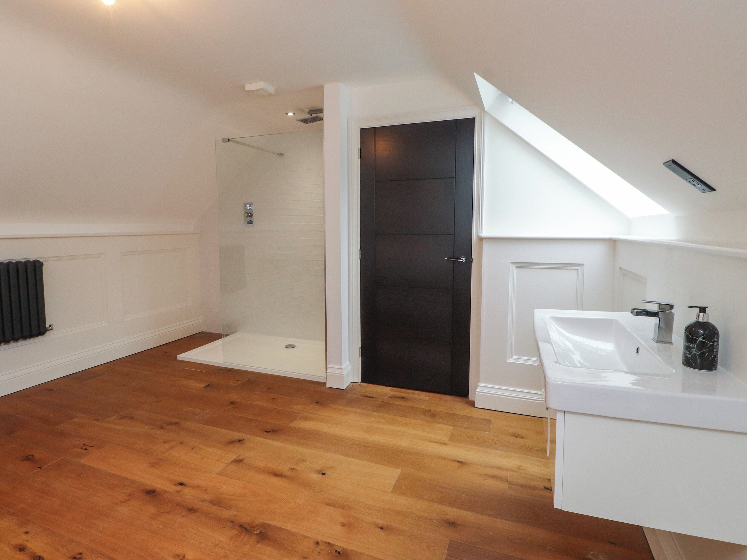 A modern bathroom with a white sink, dark door, and a glass shower enclosure.