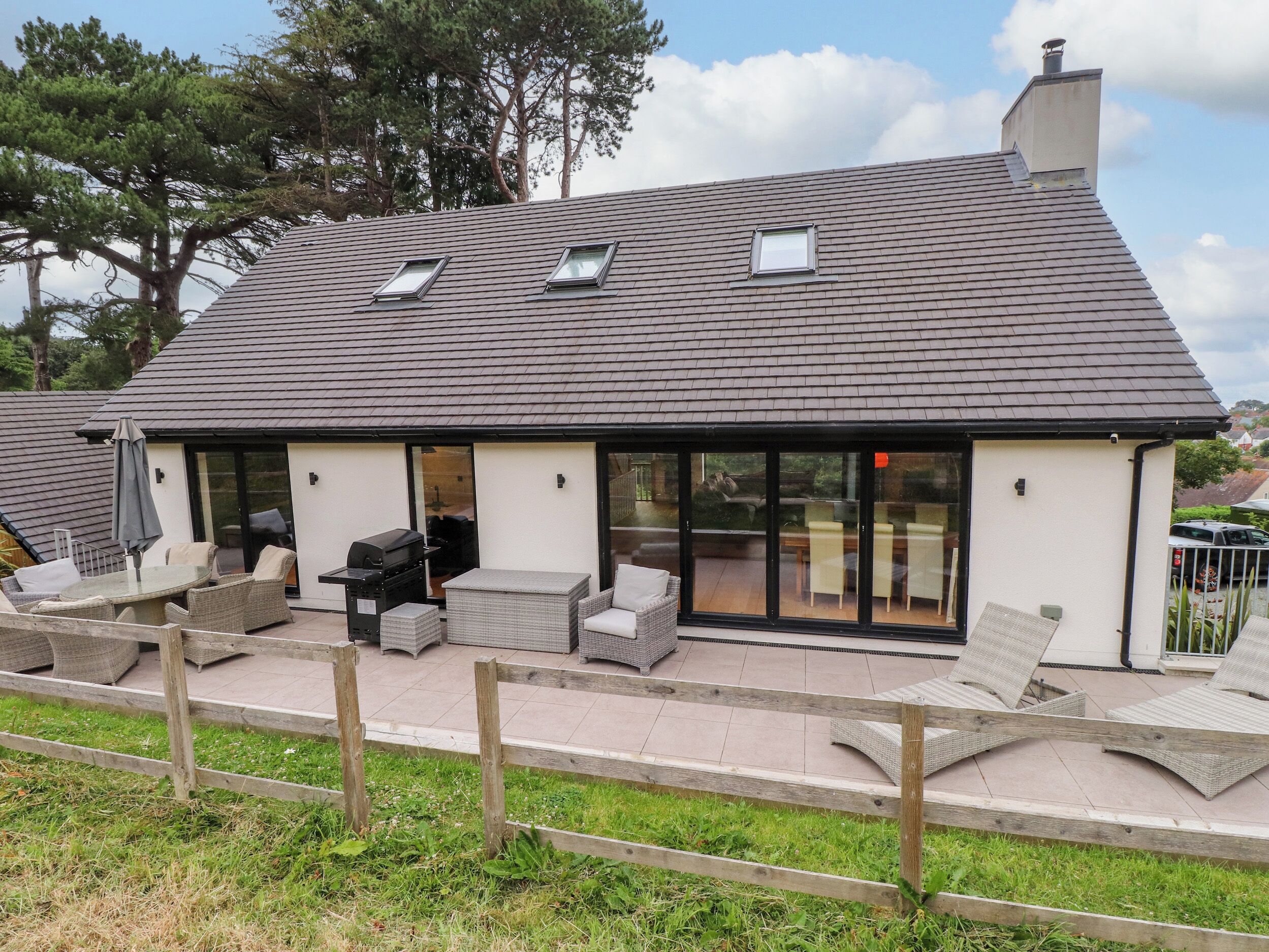 A house with a sloped roof, large glass doors, outdoor seating, and a chimney.