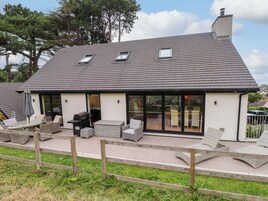 Una casa con techo inclinado, amplias puertas de cristal, mobiliario exterior y una chimenea.