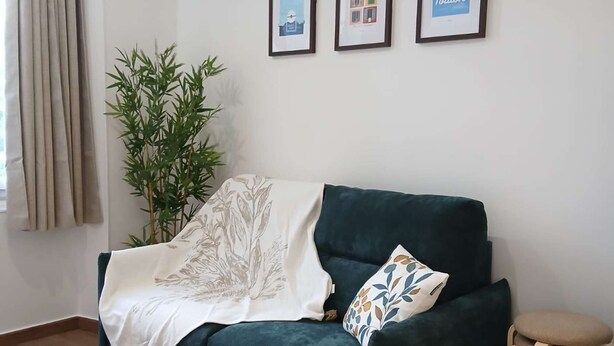 A living room with a dark green sofa, a white throw blanket, a small round wooden stool, and a bamboo plant. There are three framed pictures on the wall. - Le Bonaparte - Charming 2-room apartment near the port of Toulon (Toulon)