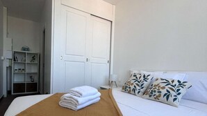 A hotel room with a bed, a wardrobe, a bedside table, and a shelf with books and a vase. - Le Bonaparte - Charming 2-room apartment near the port of Toulon (Toulon)