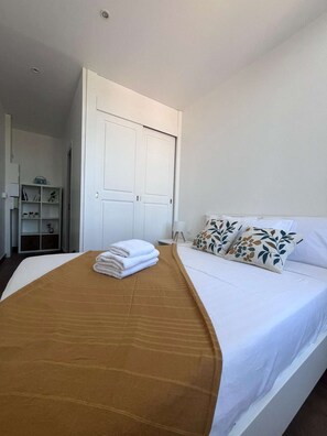 Ein Hotelzimmer mit Bett, Kleiderschrank, Nachttisch und einem Regal mit Büchern und einer Vase.
