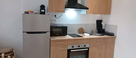 Una cocina compacta con refrigerador, microondas, estufa y armarios de madera.