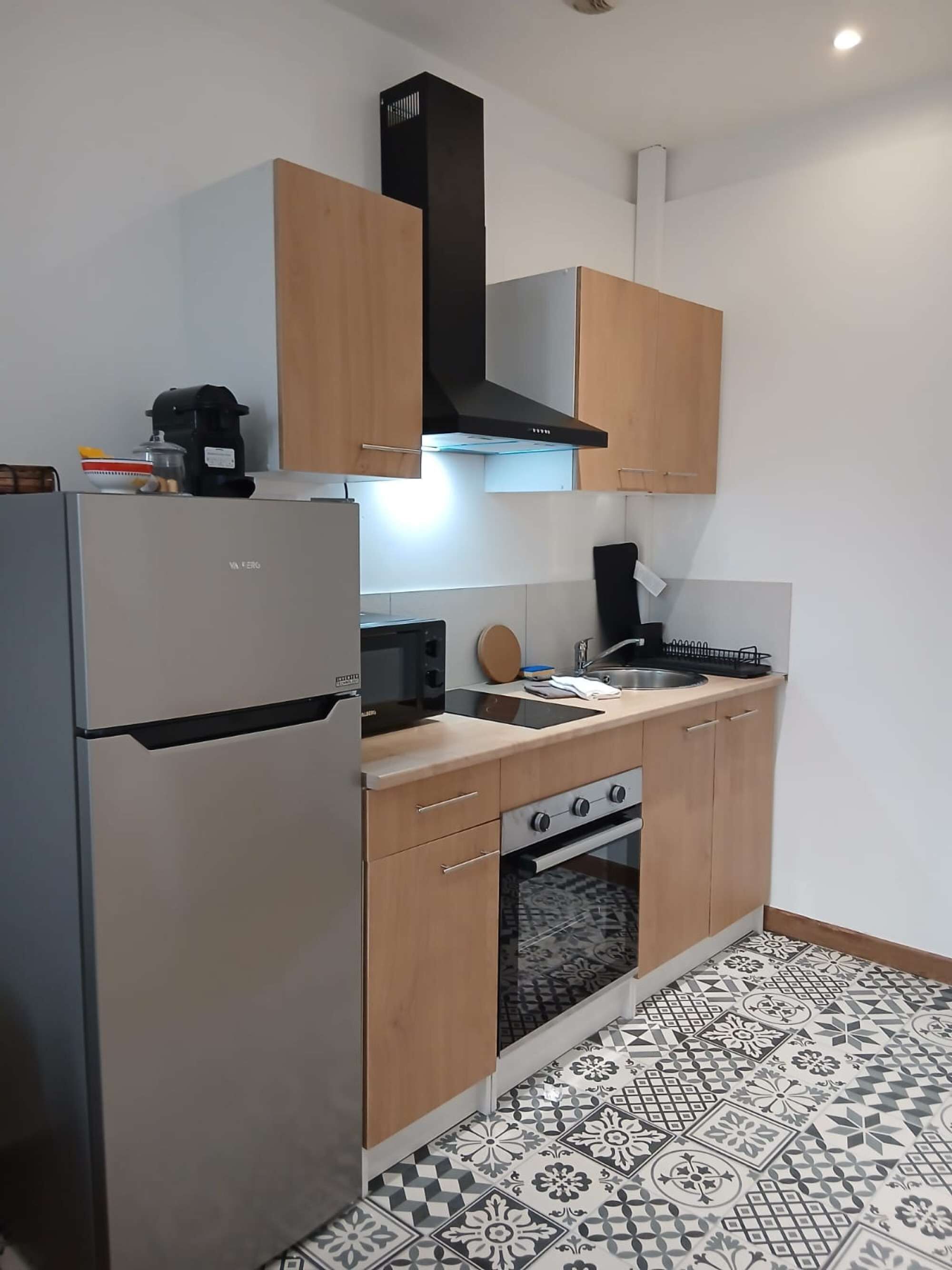 A compact kitchen with a refrigerator, stove, oven, and a coffee maker on the countertop.