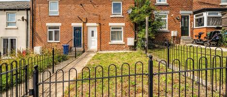 A residential brick house with a front yard, a metal fence, and a parked scooter.