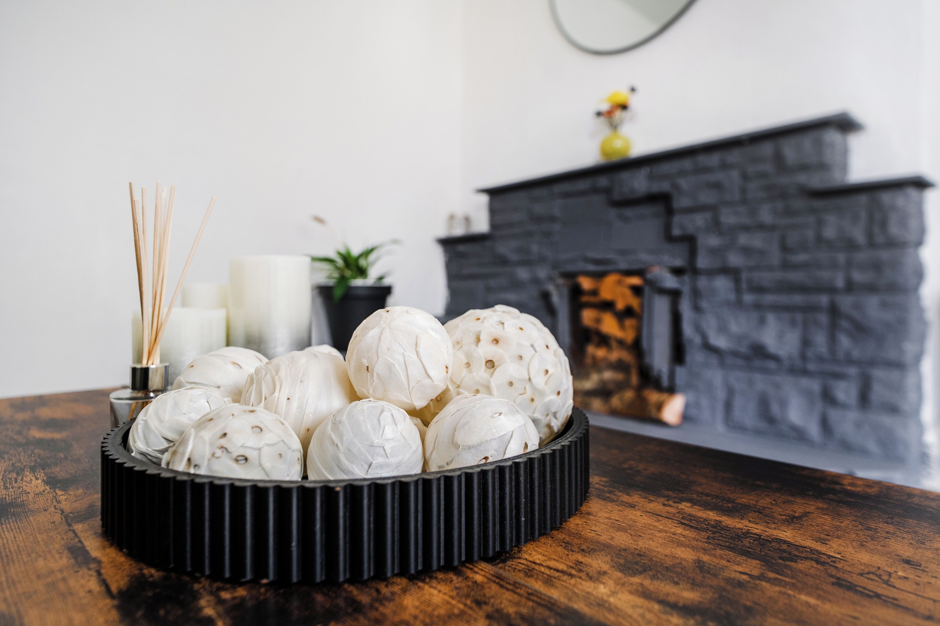 A black tray with white spherical objects on a wooden table, a white candle, and reed diffusers in the background.