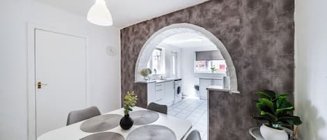 A modern kitchen with a central island, a dining area with a white table and grey placemats, and a grey textured wall.