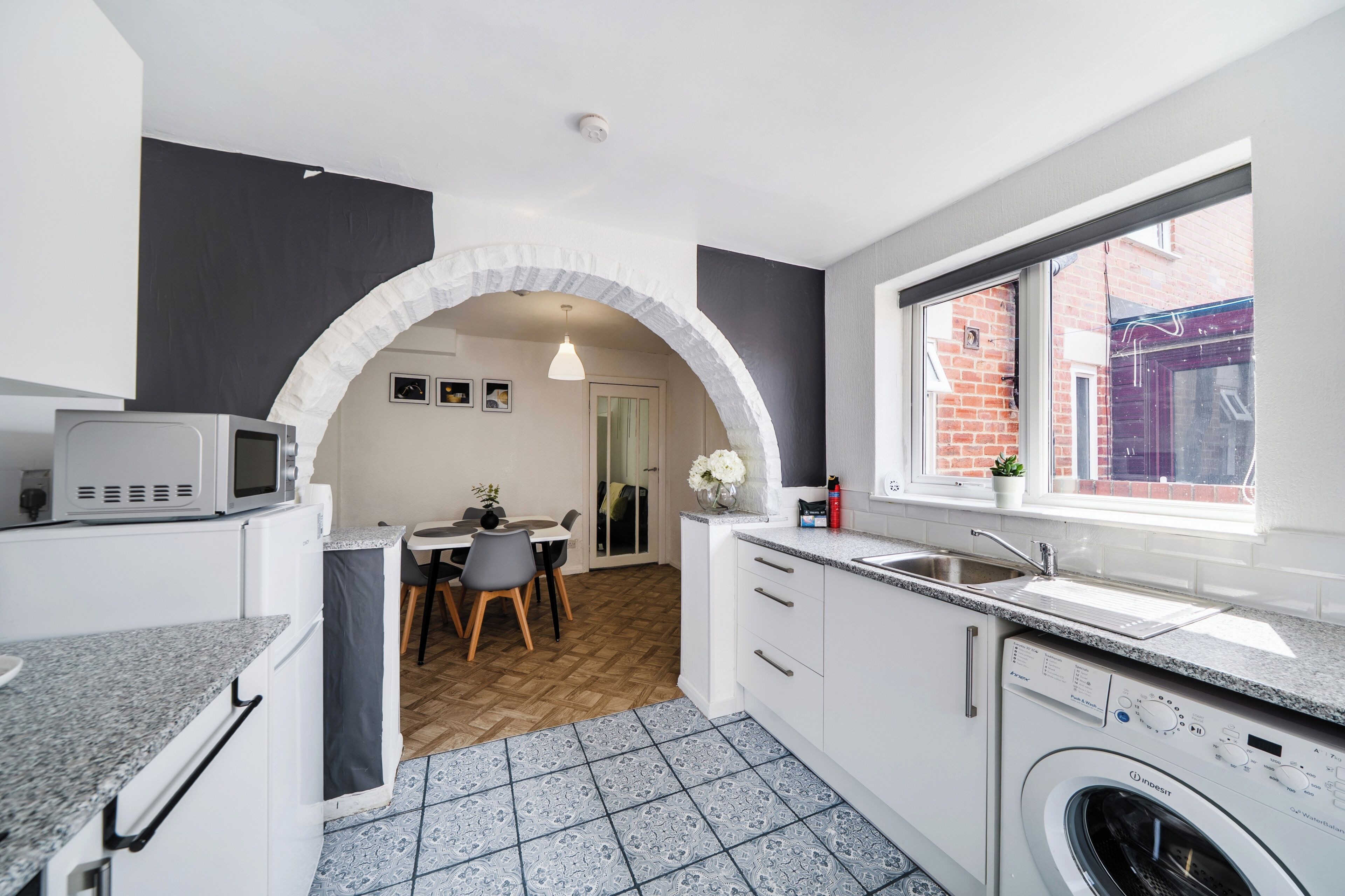 A compact kitchen with a washing machine, a microwave, and a dining area with a table and chairs.