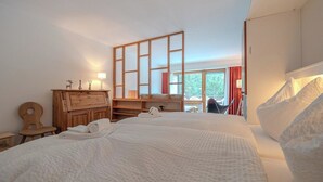 Quarto com cama grande, cómoda de madeira e janela com vista para árvores.