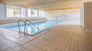 Uma piscina interior com chão em mosaico, teto de madeira e um mural na parede.