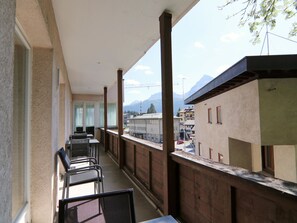 Een balkon met stoelen en tafels, uitzicht op gebouwen en bergen, en een heldere lucht.