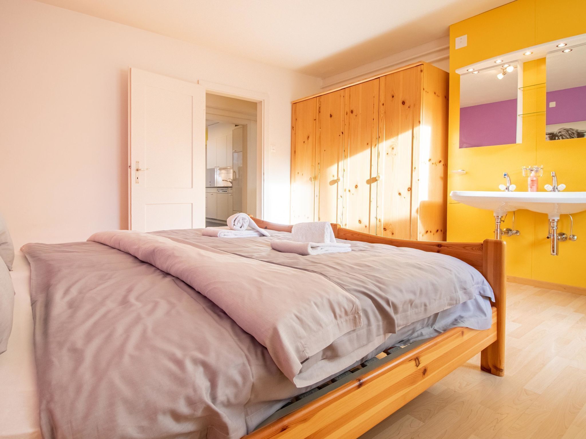 Een slaapkamer met een bed, een houten garderobe en een badkamer met een wastafel.